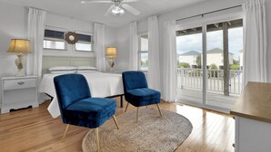 A bedroom with a bed, two blue chairs, a ceiling fan, and a large window with curtains. - Ocean Escape with Private Beach Access & Coastal Comforts (Surf City)