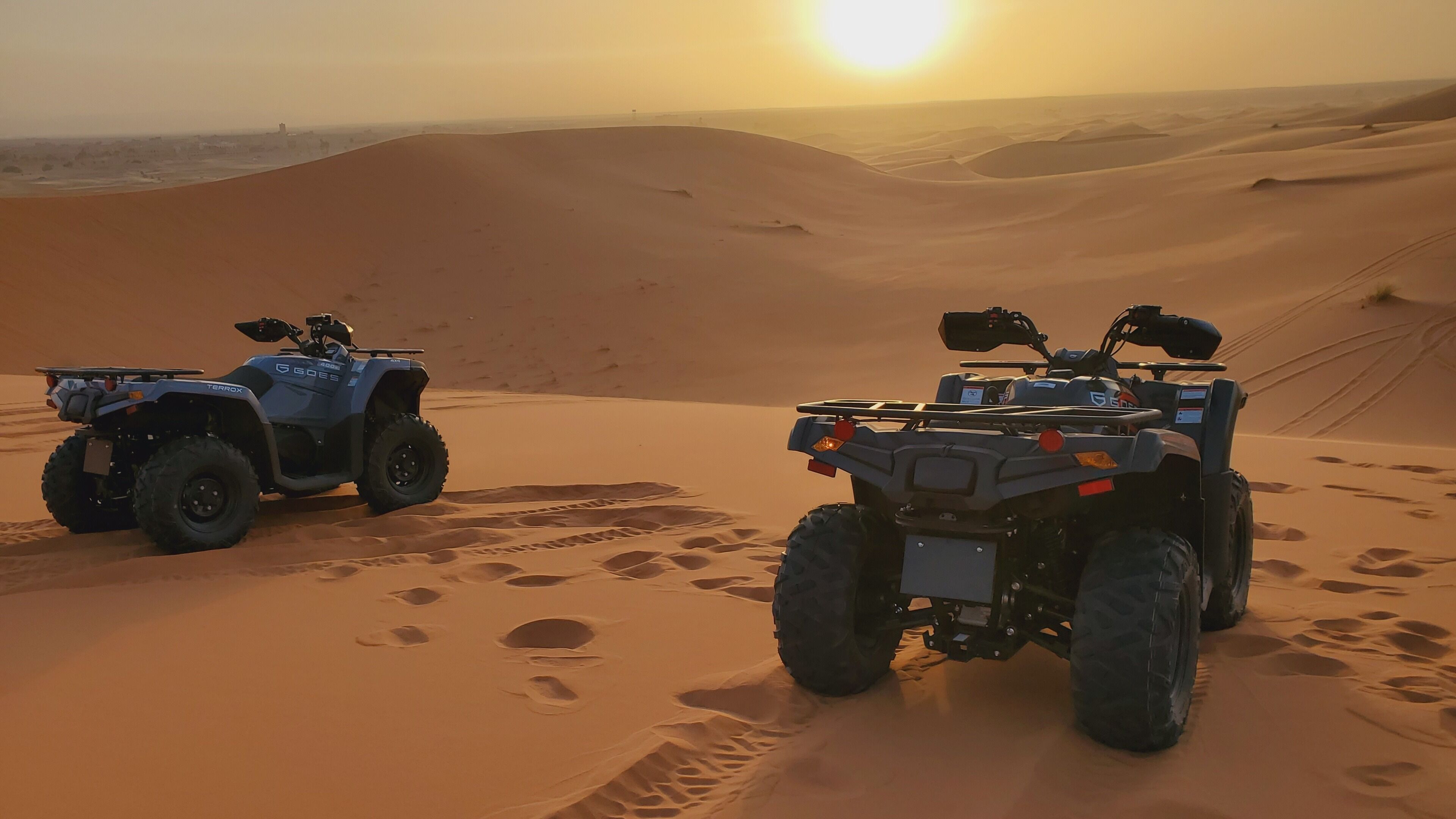 Dos quads estacionats a un turó de sorra amb un sol de tramuntana al fons.