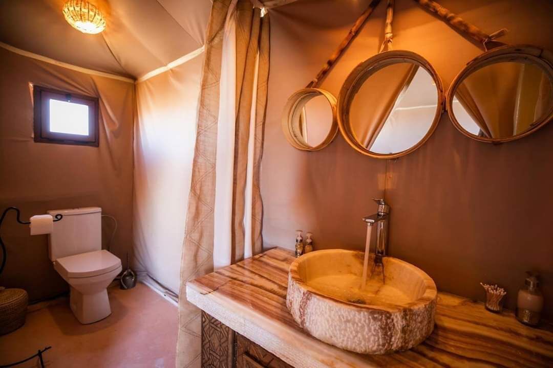 Un baño con tocador de madera, un lavabo redondo y dos espejos fijos en la pared.