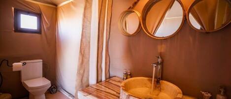 Un baño con tocador de madera, un lavabo redondo y dos espejos fijos en la pared.