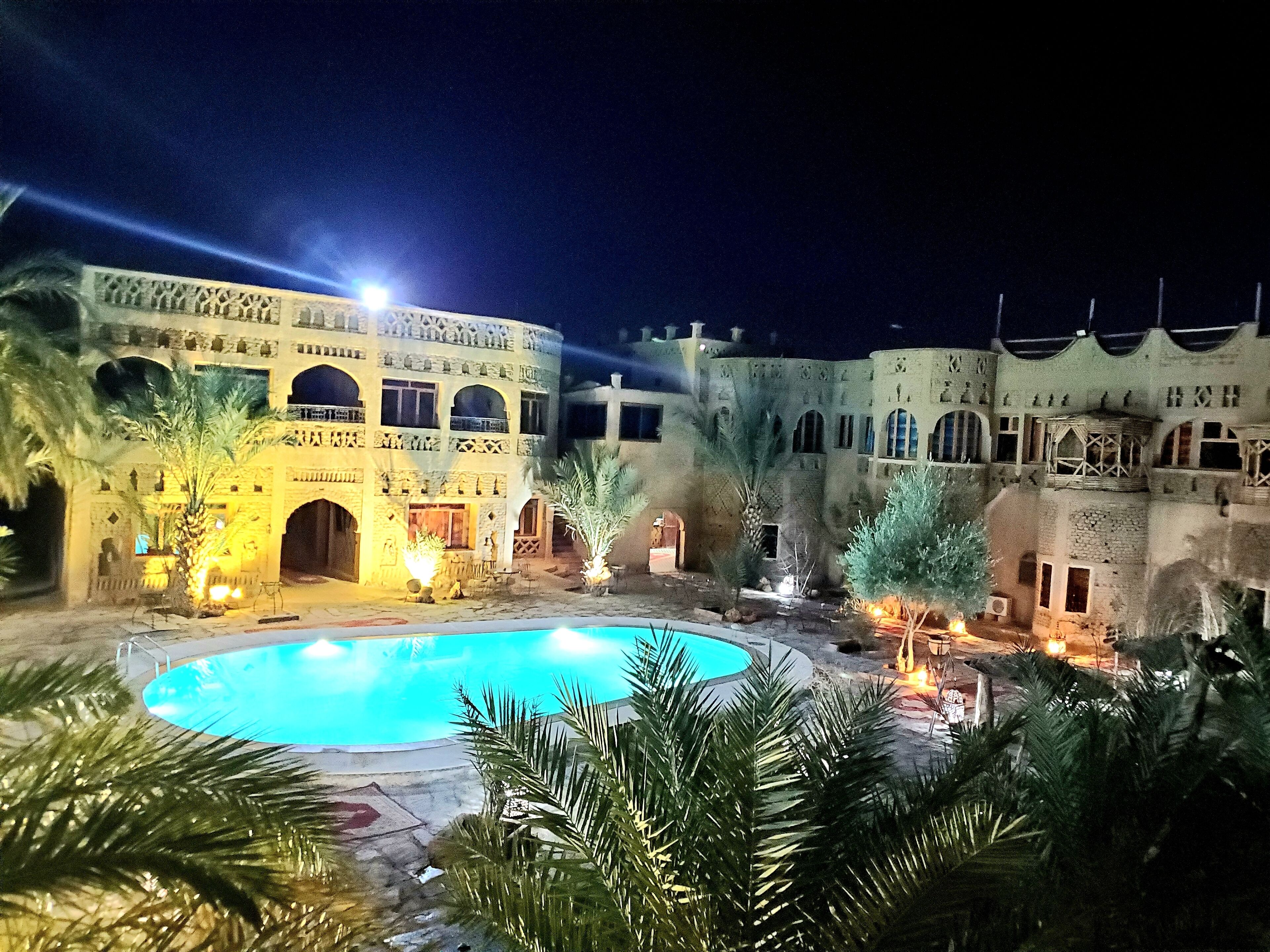 Un patio con piscina, palmeras y un edificio con arcos y una fuente.