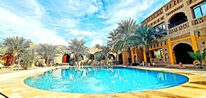Una piscina a forma curva, circondata da palme e un edificio con archi e balconi.