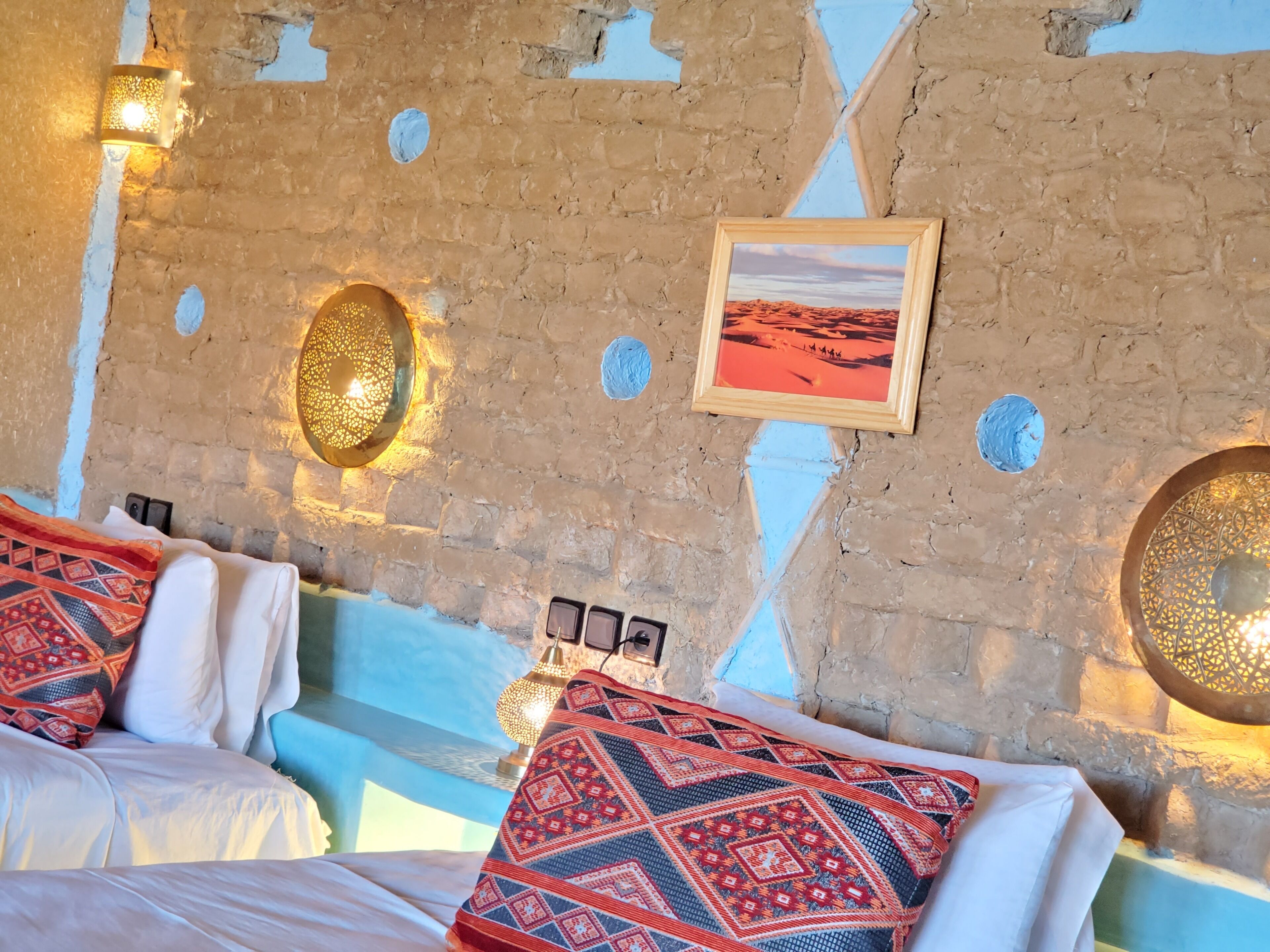 Une pièce avec un mur en briques, un tableau encadré et un plaid à motifs sur le lit.