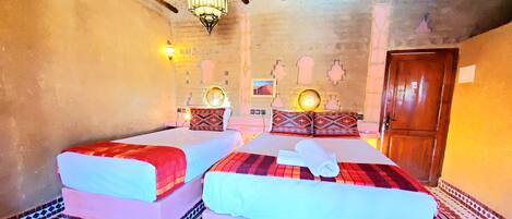 A room with two beds, patterned rugs, a chandelier, and a wooden door.