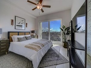 Quarto com cama, mesa de cabeceira, ventilador de teto, janela grande e vista para o exterior.