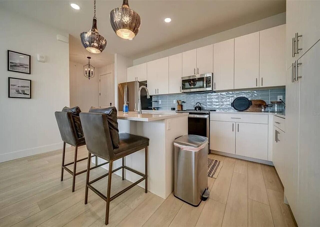 Una cocina moderna con armarios blancos, un cubo de basura de acero inoxidable y una zona de bar con dos sillas.