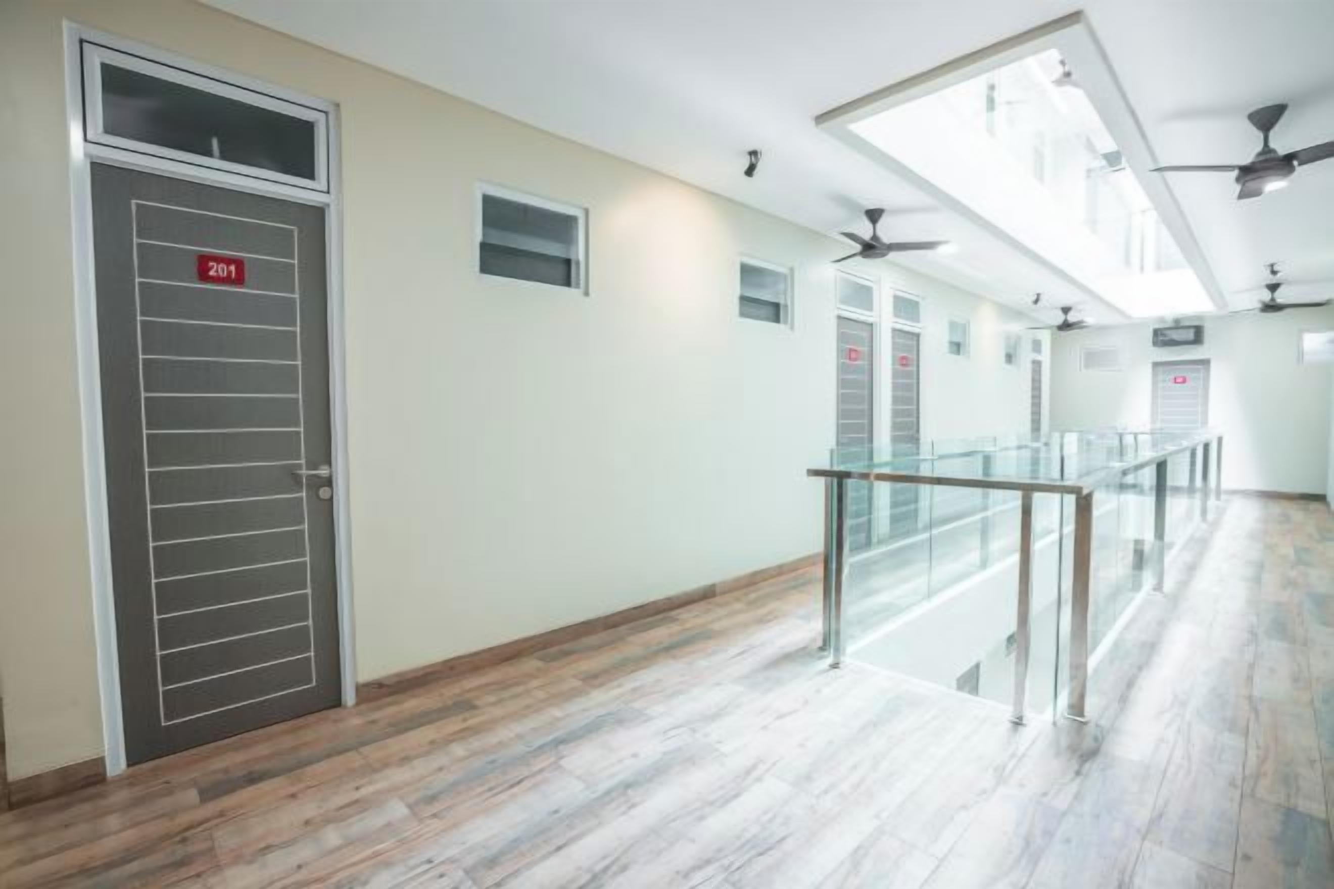 Een hotelgang met een deur met het nummer 201, een glazen balustrade en plafondventilatoren.