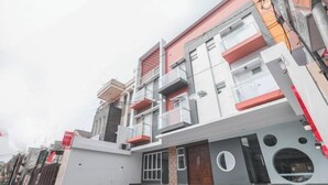 Un edificio moderno de varios pisos con balcones, una entrada porticada y un patio empedrado.