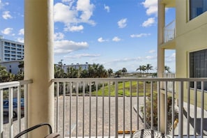 Un balcon donnant sur une zone pavée, des palmiers et des bâtiments en arrière-plan.