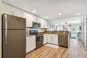 Une cuisine moderne dotée d’appareils électroménagers en acier inoxydable, de meubles blancs et d’un plancher en bois.