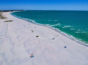 Une vaste plage de sable fin, bordée d’une eau turquoise et cristalline, et parsemée de quelques parasols.