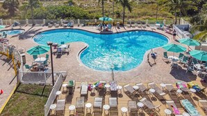 Una piscina grande y curva con sillones de descanso y sombrillas, rodeada por una terraza y vistas a la playa y al océano.