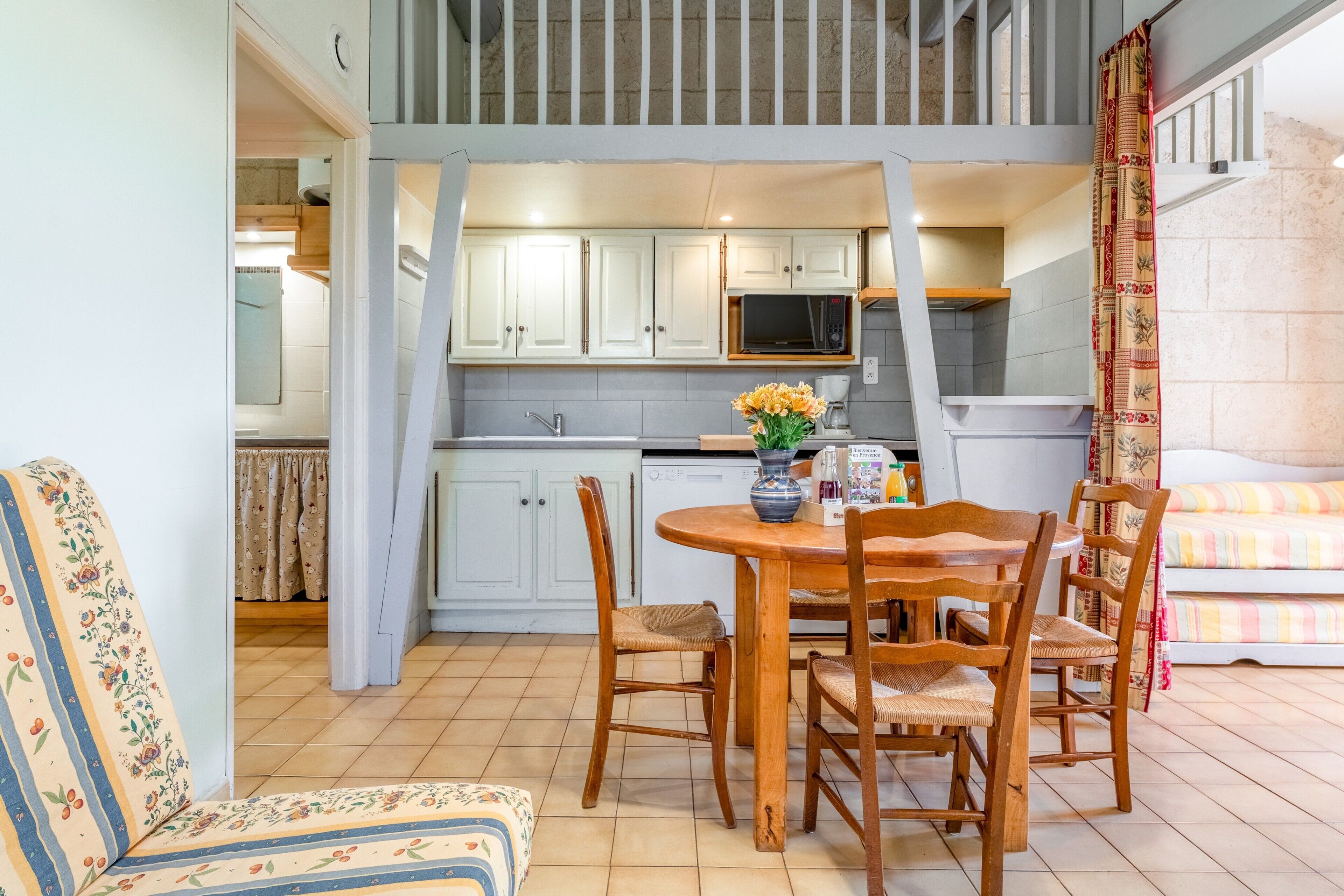 Un comedor con una mesa y sillas de madera, una cocina al fondo y una escalera que sube a un nivel superior.