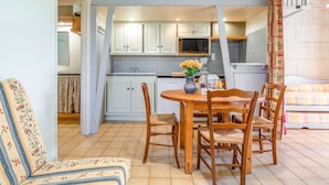 A dining area with a wooden table and chairs, a kitchen in the background, and a staircase leading to an upper level. - Holiday Home 'Gite Fontenelle Alpilles' with Shared Pool, Wi-Fi & Air Conditioning (Arles)