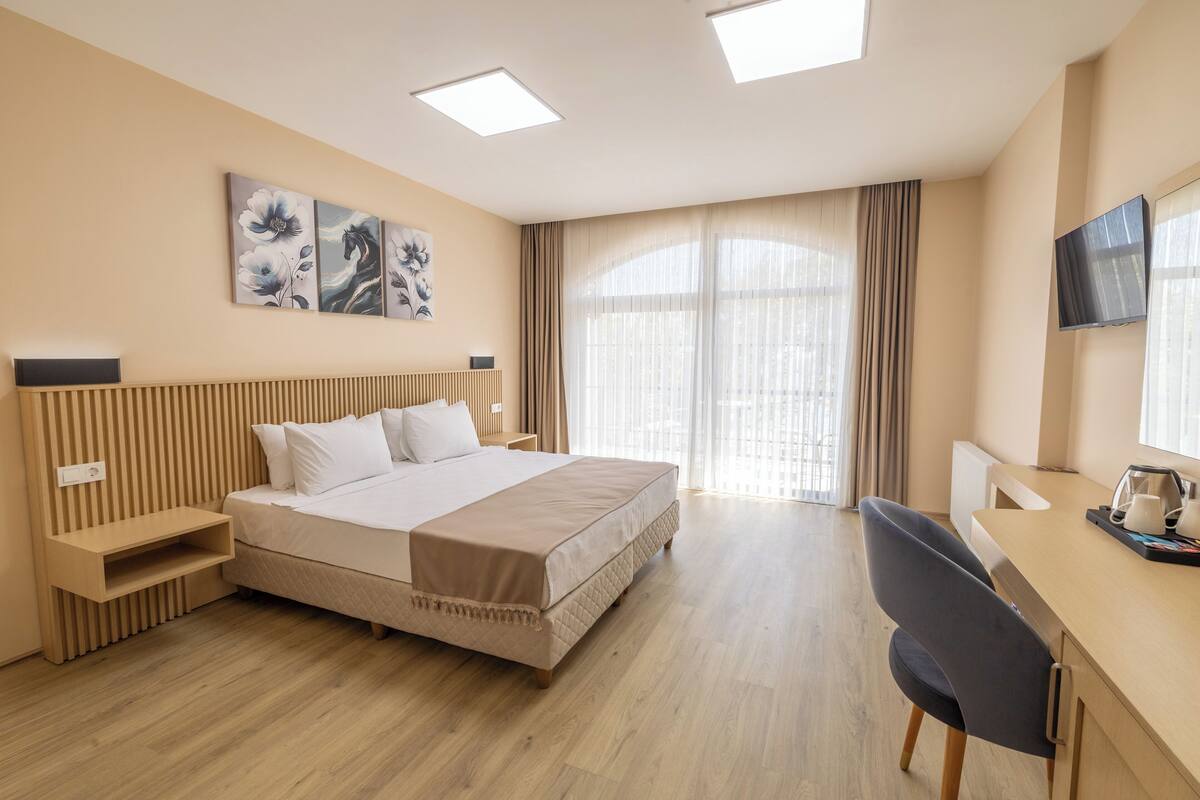 A modern hotel room with a large bed, bedside tables, a desk with a chair, and artwork on the wall.