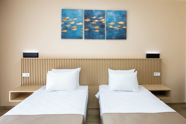 Quarto de hotel com duas camas de solteiro, cabeceira de madeira e uma pintura de peixes na parede.