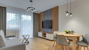 A modern living room with a sofa, dining table, chairs, and a TV. - Seaside Latarników by Downtown Apartments (Gdańsk)