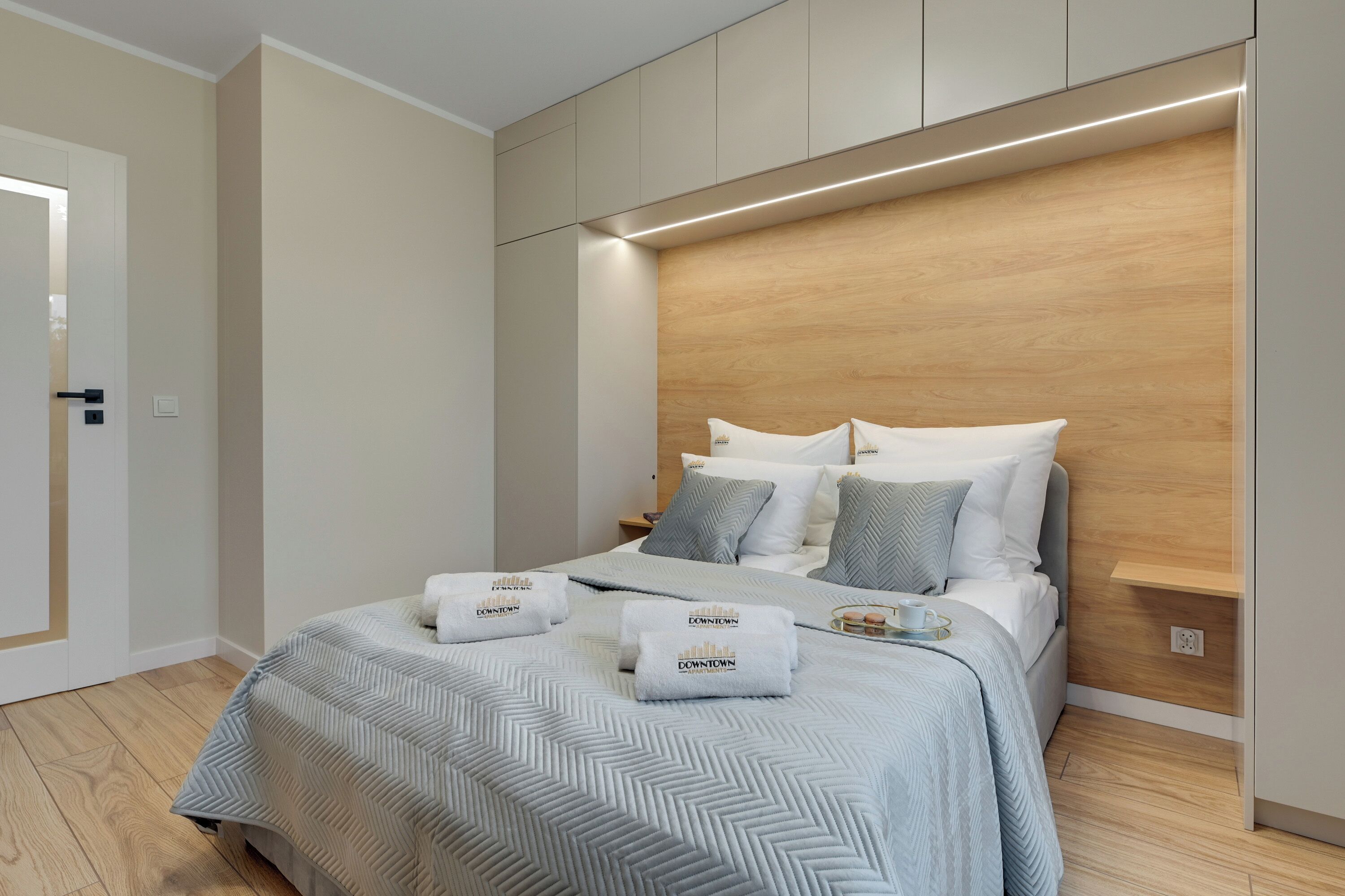 A modern hotel room with a large bed, wooden headboard, and a small bedside table with a cup and saucer.