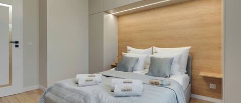 A modern hotel room with a large bed, wooden headboard, and a small bedside table with a cup and saucer.