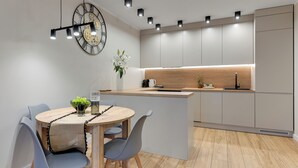 A modern kitchen with a central island, pendant lighting, and a clock on the wall. - Seaside Latarników by Downtown Apartments (Gdańsk)