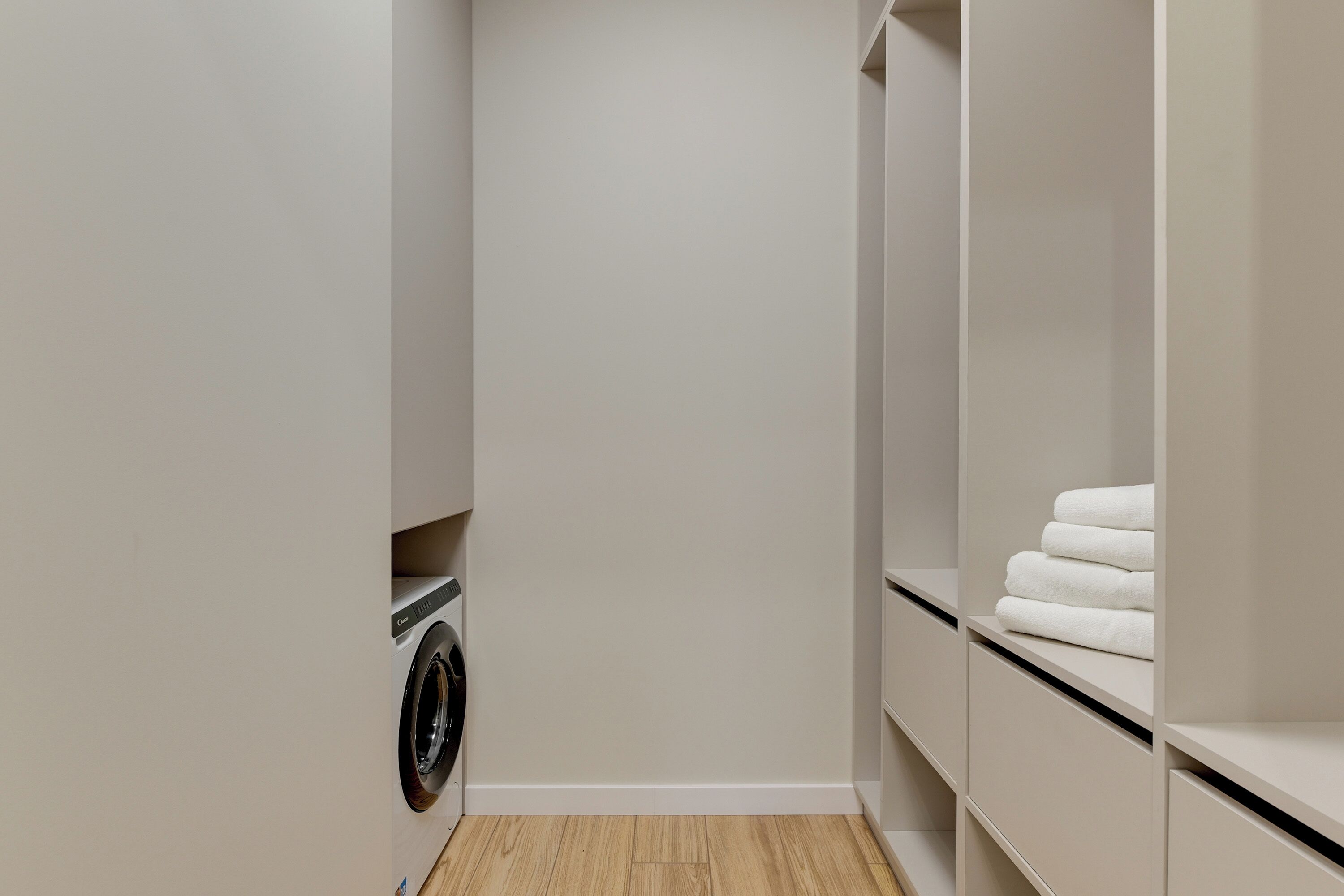 A laundry room with a washing machine, a dryer, and shelves with folded towels.