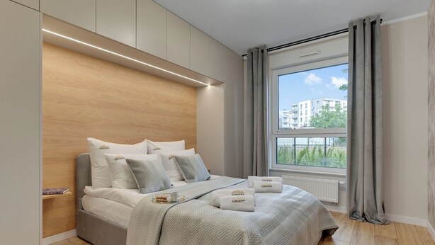A modern bedroom with a large bed, grey bedding, a bedside table with a tray, and a window with curtains. - Seaside Latarników by Downtown Apartments (Gdańsk)