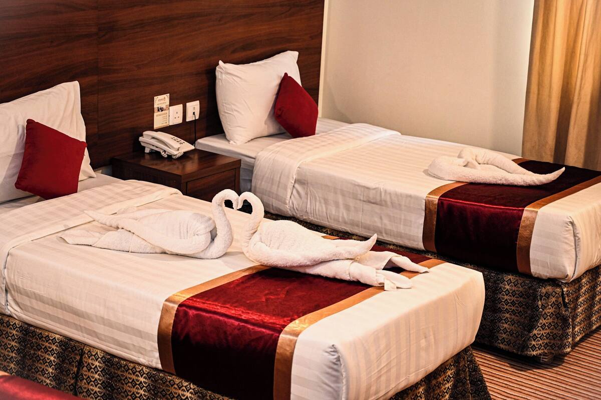 A hotel room with two beds, each with a red and white pillow, a telephone on the nightstand, and a red and gold bedspread.