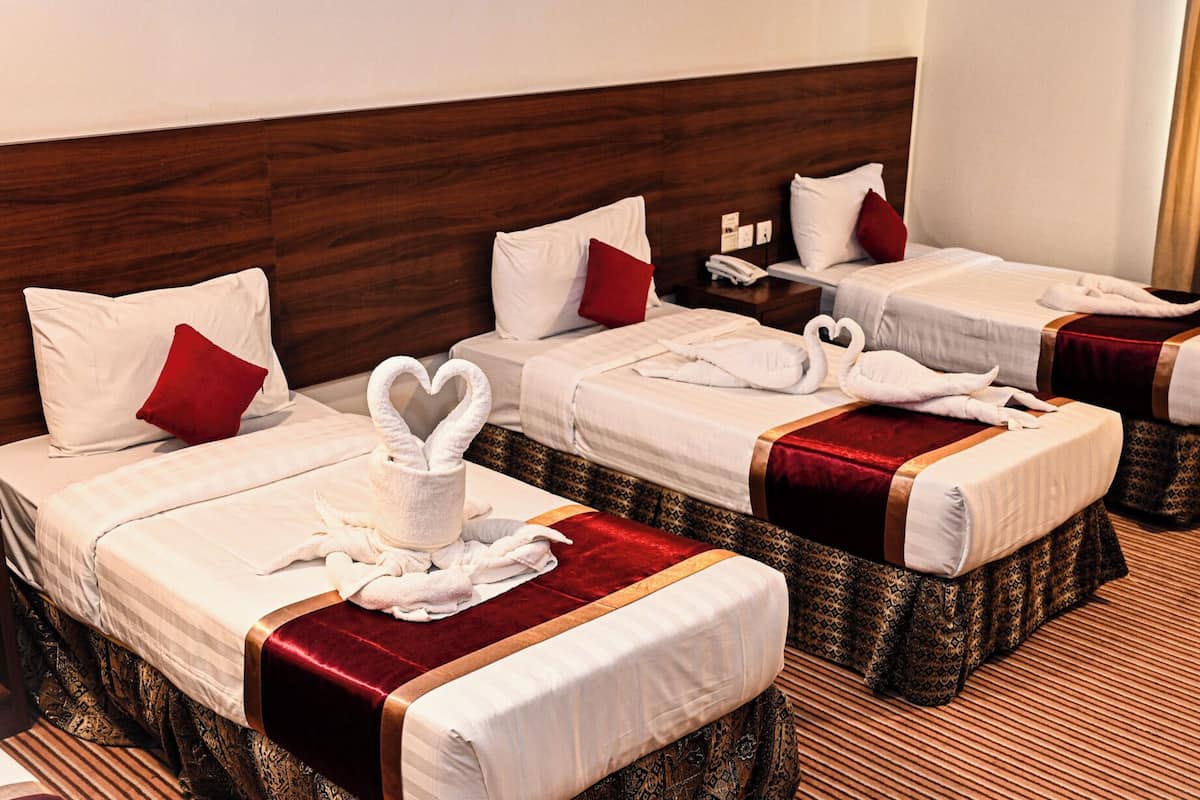 A hotel room with three beds, each with a heart-shaped towel and a red pillow.