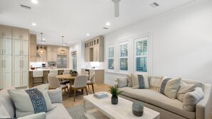 Una sala moderna con un sofá color beige, una mesa de centro y un comedor con cocina al fondo.