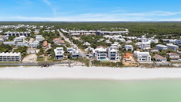Vista aérea de una zona residencial costera con casas, una playa y un fondo arbolado.