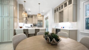 Una cocina moderna con armarios de madera clara, una isla central con sillas, luces colgantes y una planta en maceta sobre la isla.