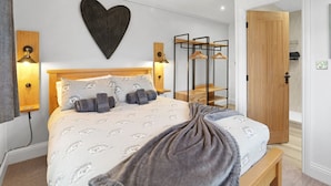 Une chambre à coucher comprenant un lit, des lampes de chevet, un élément de décoration murale en forme de cœur, une armoire et un banc.
