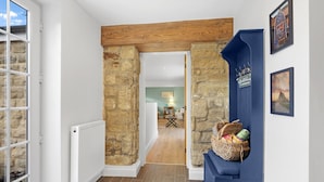 Un couloir aux murs de pierre, au plafond en bois et où se trouve un banc bleu avec un panier.