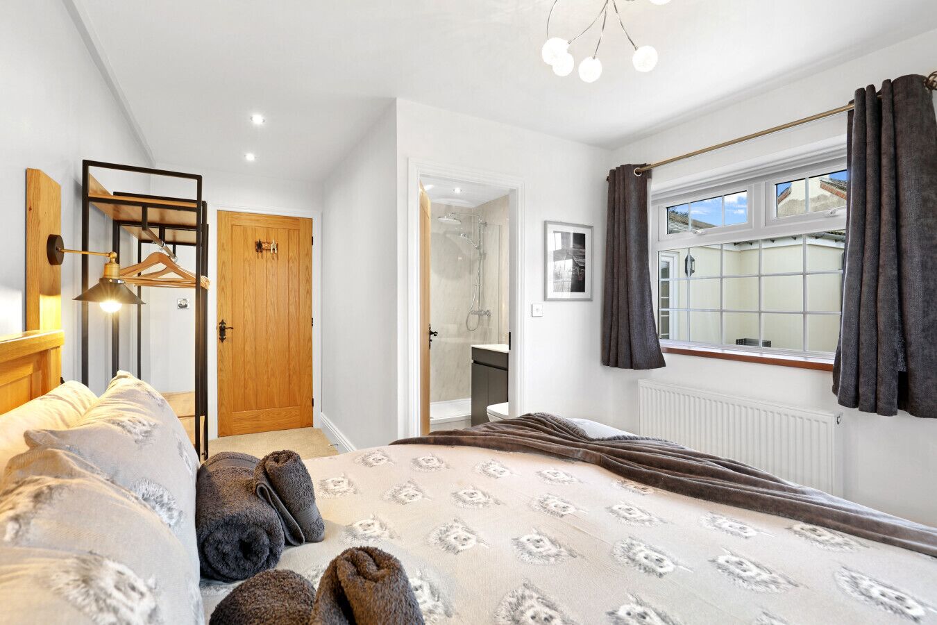 A bedroom with a bed, a wardrobe, a mirror, a window with curtains, and a bathroom visible through an open door.