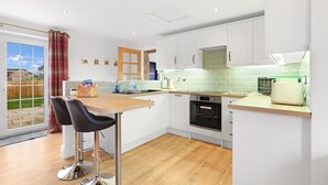 Une cuisine moderne avec des armoires blanches, un plan de travail en bois et un four encastré. On y trouve également un coin repas avec deux chaises noires et une table.