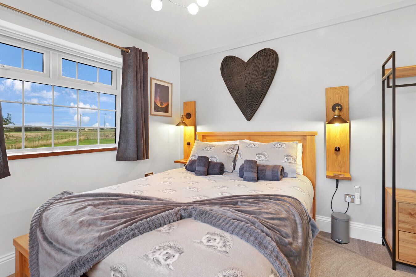 Een slaapkamer met een groot bed, uitzicht op de natuur, een hartvormige decoratie aan de wand en twee wandlampen.
