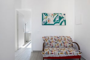 Une pièce avec un canapé à motifs, une œuvre d’art murale et une porte donnant sur une autre pièce.