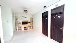 A hallway with a ceiling fan, a TV on a wooden stand, and two dark doors with numbers above them. - Semarang Inn Syariah (Gayamsari)