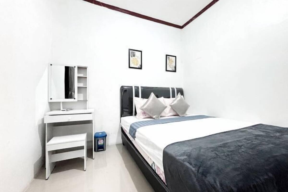 A bedroom with a bed, a desk, a chair, a small trash bin, and two framed pictures on the wall.