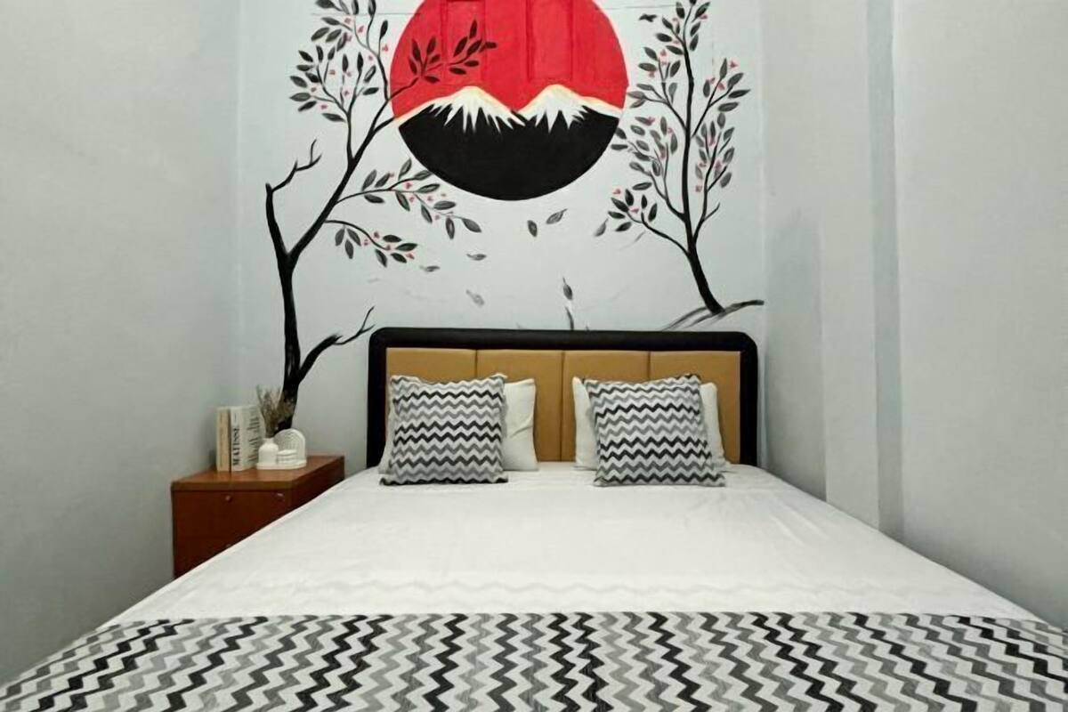 A bed with a patterned bedspread, two pillows with zigzag patterns, and a wall with a red circle and black and white tree branches.