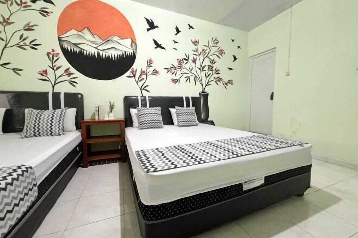 A double bed with a patterned bedspread, two bedside tables, and a wall mural.