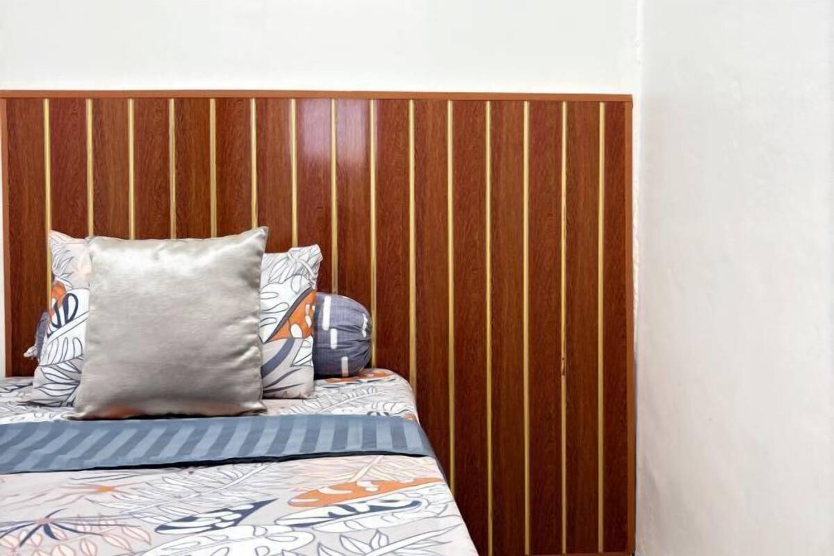 A bed with a patterned bedspread, a large pillow, and a headboard with vertical wooden slats.