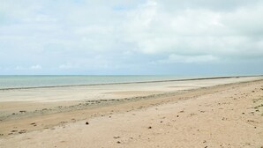 Une vaste plage de sable fin, avec une mer calme et un ciel nuageux.