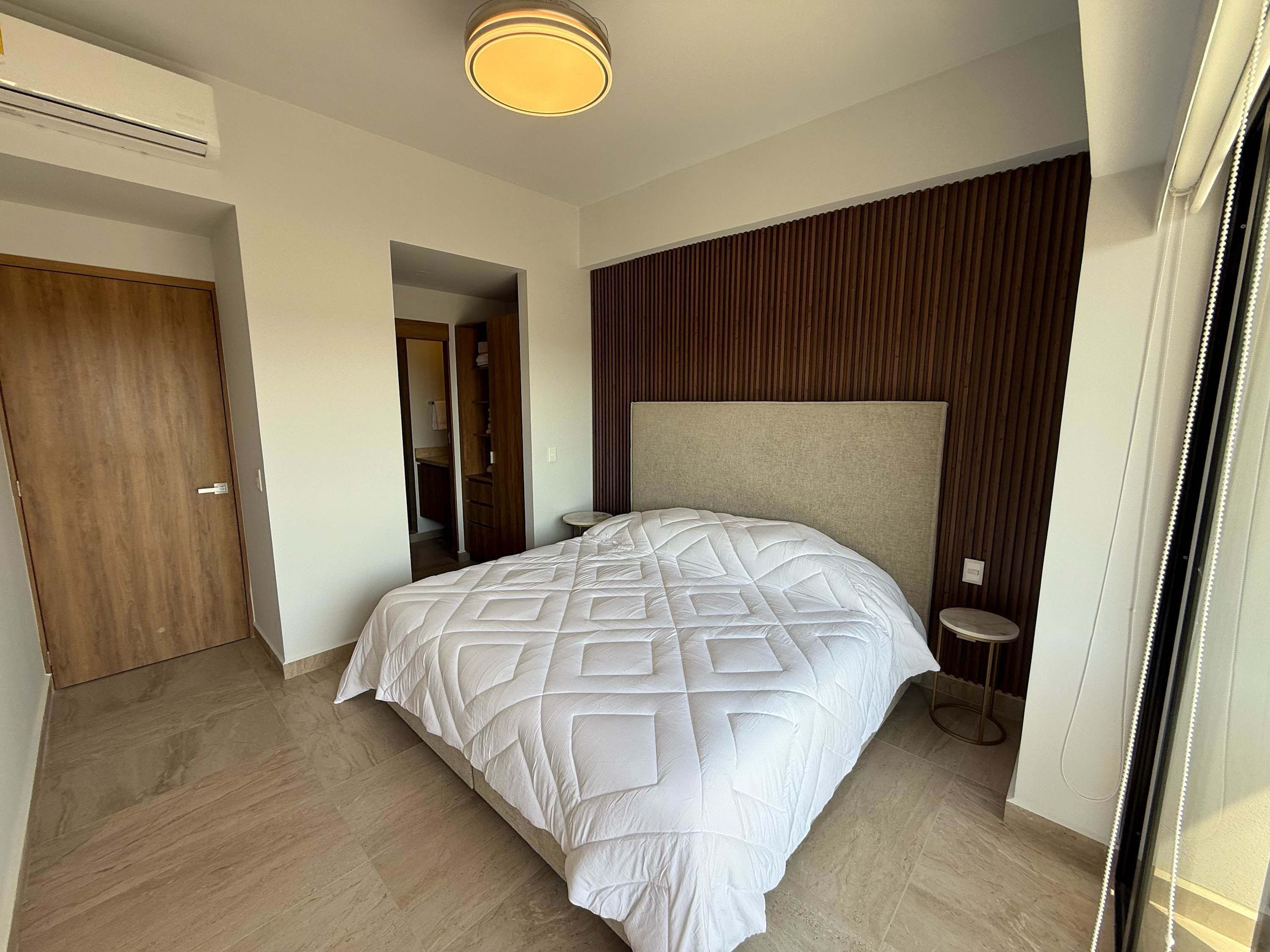 Een moderne slaapkamer met een groot bed, een houten garderobe, een inloopkast en een klein nachtkastje.