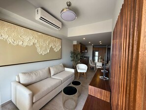 Ein modernes Wohnzimmer mit einer Couch, einem Esstisch mit Stühlen, einer Küchenzeile und einer Klimaanlage.