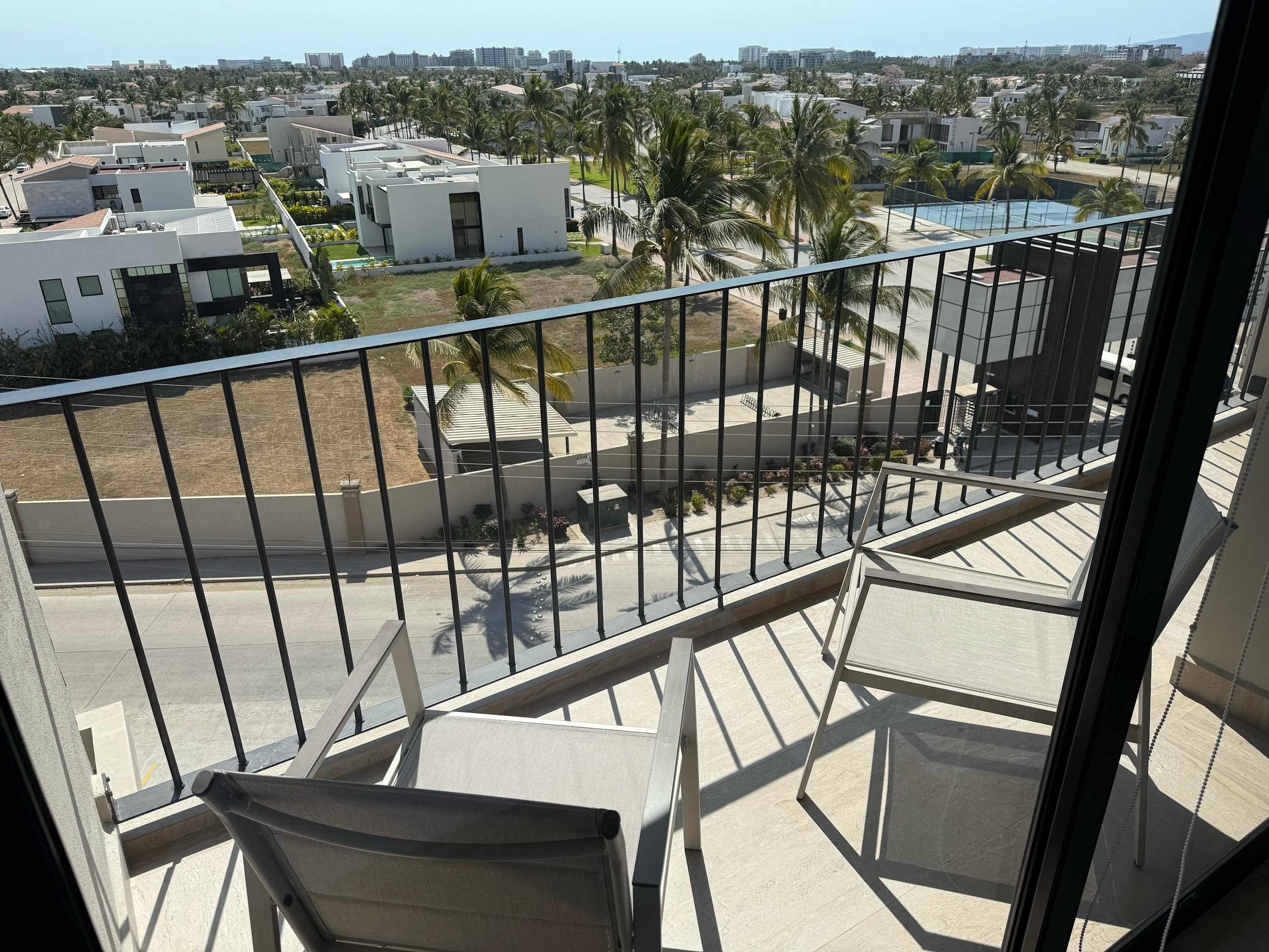 Un balcon donnant sur un quartier résidentiel, avec des immeubles modernes et des palmiers.