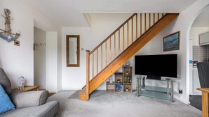 A living room with a wooden staircase, a flat-screen TV, and a glass shelf. - Quai Des Pecheurs - With Views from Bedroom Overlooking the Harbour (Poole)