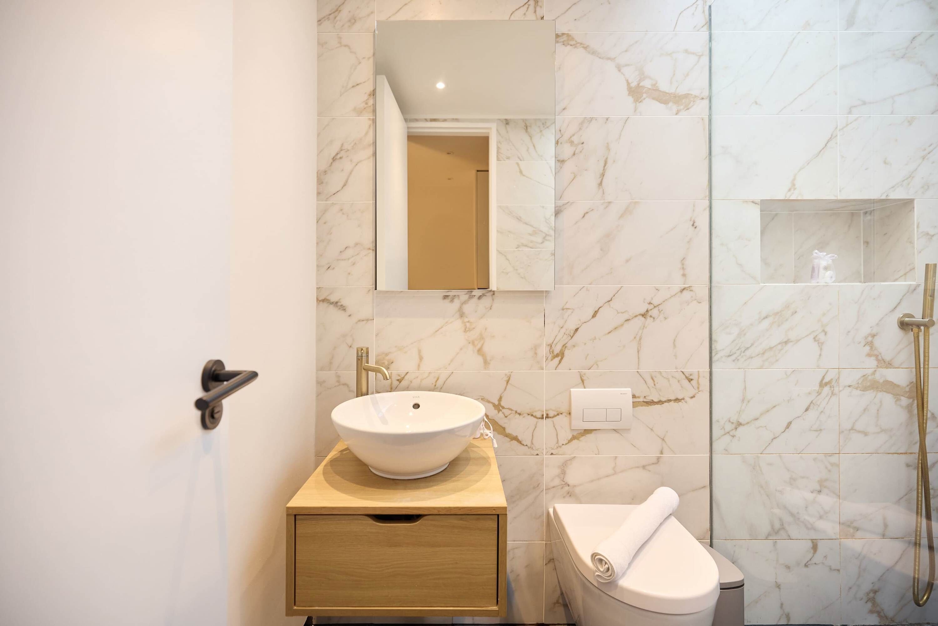 Un baño con pared de mármol, un lavamanos sobre encimera, un inodoro y una ducha.