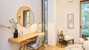 Een moderne slaapkamer met een houten bureau, een ronde spiegel, een stoel, een klein tafeltje en een bed.