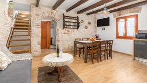 Um interior rústico com escada de madeira, sala de jantar com mesa e cadeiras, e cozinha com televisão e janela.